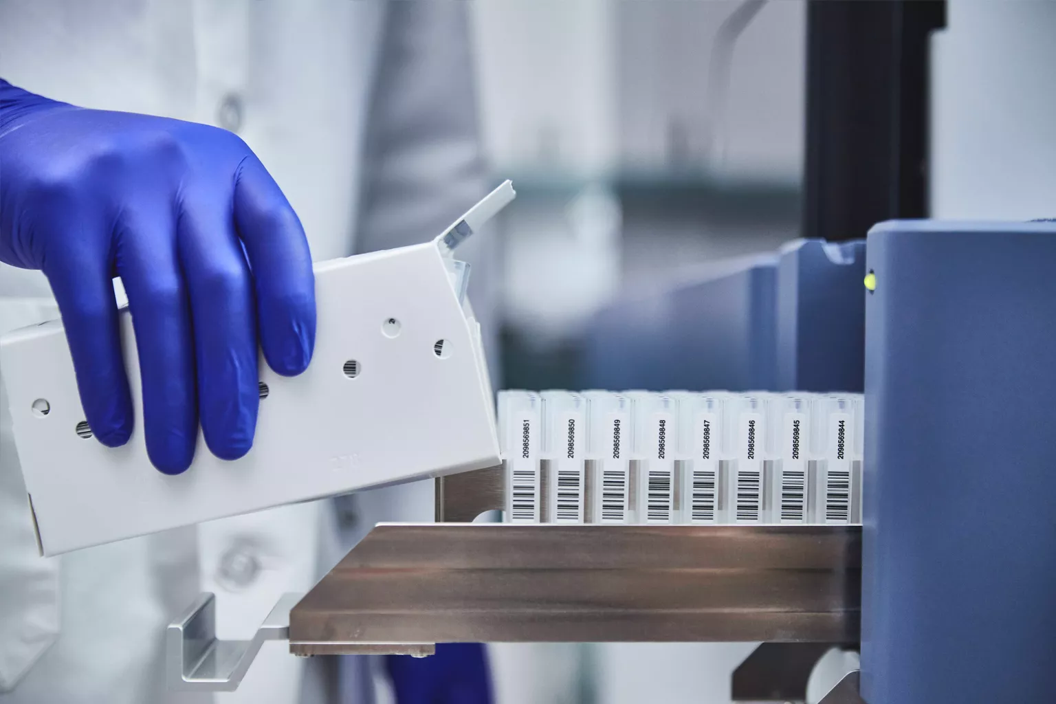 Laboratorietekniker isætter bakke med rør på et laboratorium.